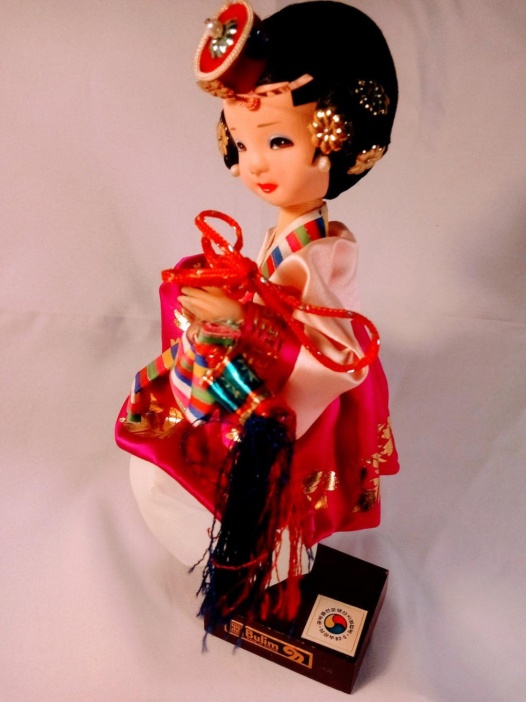 Traditional Korean doll in a red and black outfit with decorative accessories on a white background